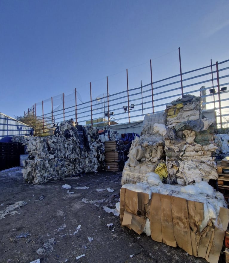 Mixed bales of waste paper and plastic in the yard under a clear blue sky