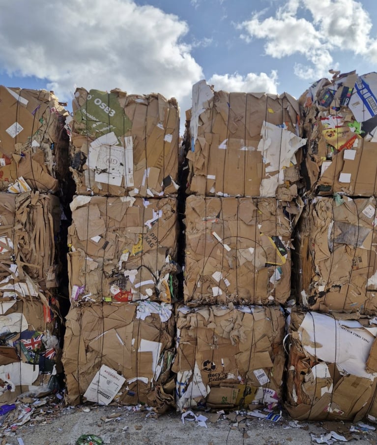 Stacked bales of cardboard in the yard under a partly cloudy sky